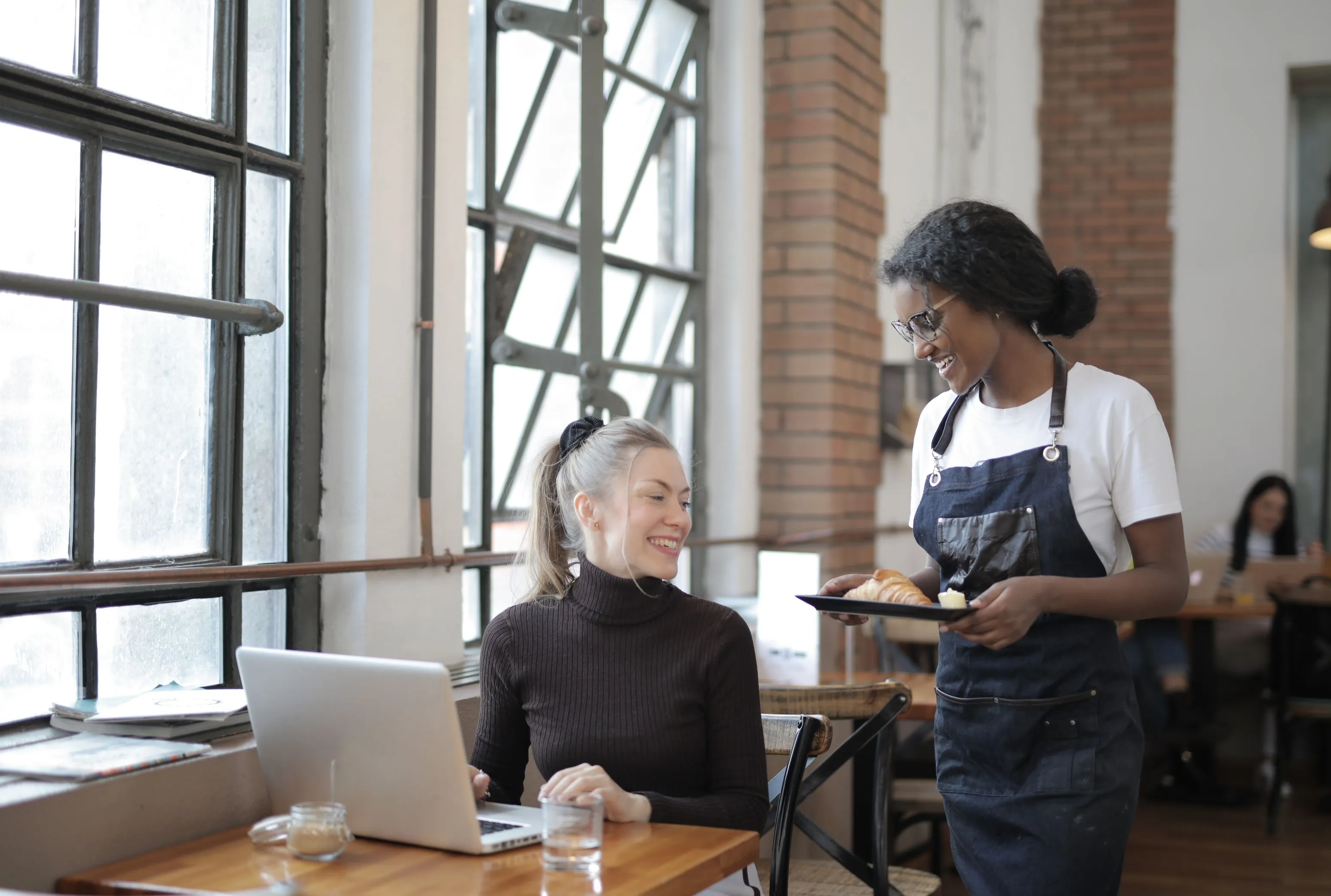 Cafe waiter serving a customer, backed by real-time POS inventory synchronization to prevent out-of-stock orders.